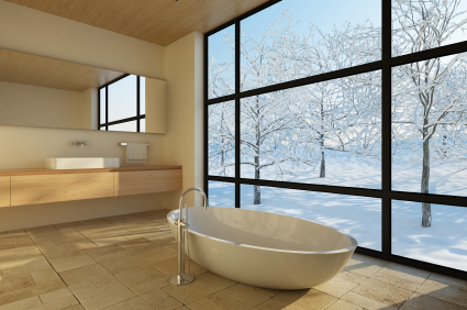 Free standing white bath in warm stone clad architect designed interior with black framed window looking out onto snowy sunlit garden typical of architects design value in macclesfield by Mark Burgess