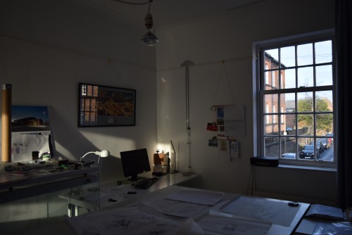 Architects Studio Macclesfield. Interior view showing sunlight falling onto desk beside window onto sunlit street.