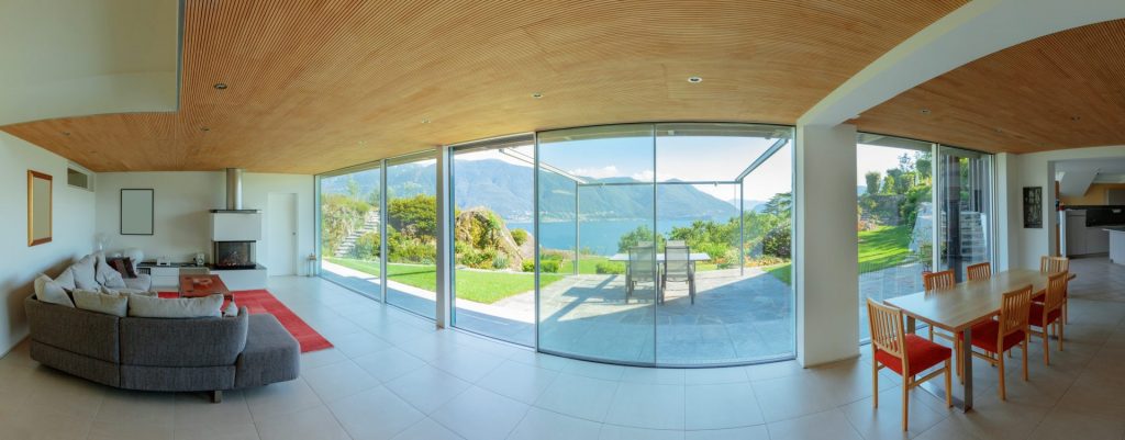 Distorted interior view so show the view outside too. Plain light-toned ceramic floor tiles and side walls. Panoramic view of Lake Maggiore and mountains beyond. Acoustically grooved wooden ceiling in this holiday home.