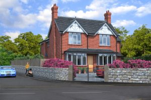Red brick Sanbach townhouse two storey with gables over windows. Trees, in leaf, behind. Purple flowering shrubs in foreground.